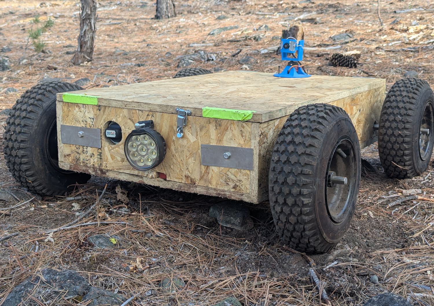The proof-of-concept machine: plywood body on four knobbly tyres, work light and a blue camera mount on top
